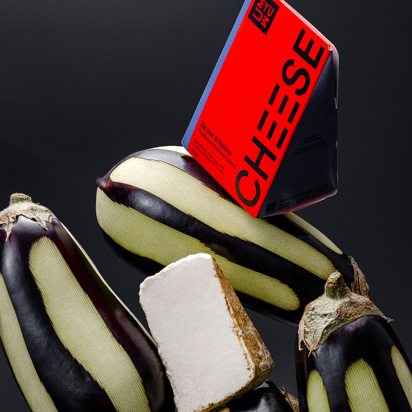 UMYUM plantbased cheese wedge and packaging displayed among striped eggplants.